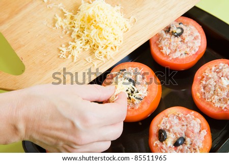 Closeup of cook adds cheese to stuffed tomato. See in series stages of cooking of stuffed tomato