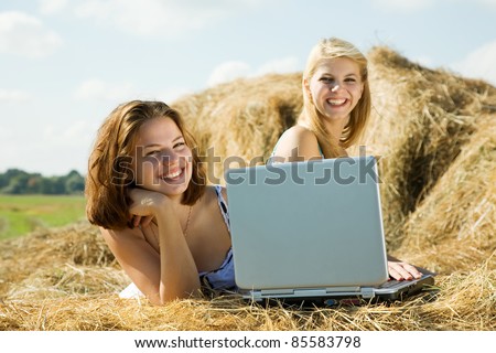 country girls restings with laptop on fresh hay bale