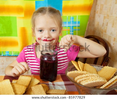 Little girl eating jam from  jar at kitchen
