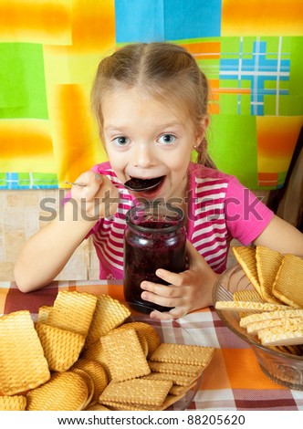 Little girl eating jam from  jar at kitchen