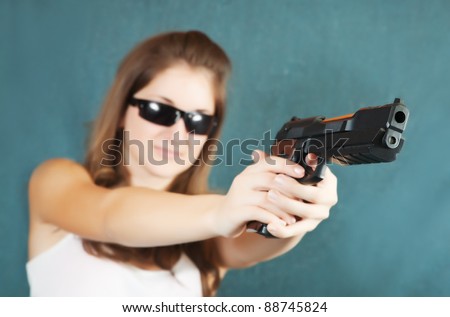 Long-haired teen girl aiming a black gun. Focus on gun only