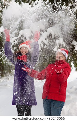 Two  young women throwing snow  in the air in park