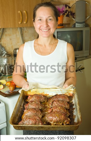 Mature woman with cooked stuffed beef on roasting pan in kitchen. One of the stages of preparation of  stuffed beef.  See series