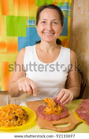 Mature woman stuffing beef by fried onion and carrot. One of the stages of preparation of the stuffed beef.  See series