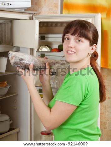 Young woman putting raw frozen fish into fridge at home