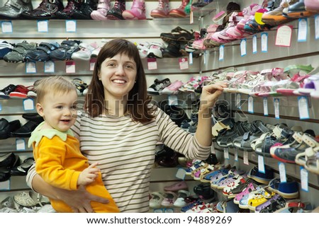 Happy mother with her child chooses baby shoes at fashionable shop