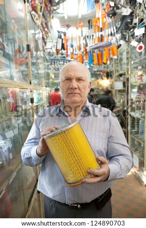 mature man holds  automotive  air filter in  auto parts store