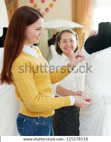 Happy mother  with daughter chooses bridal gown at shop of wedding fashion. Focus on bride