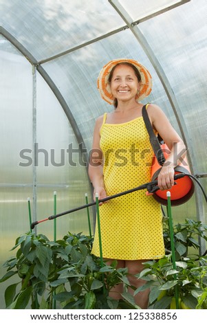 Female gardener working in greenhouse with knapsack garden spray