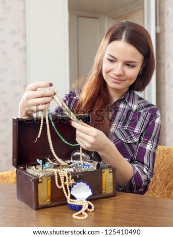 pretty girl chooses jewelry in treasure chest at home