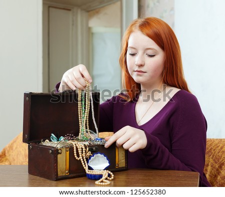 portrait of teen girl chooses jewelry in treasure chest at home