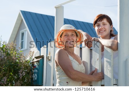 Two happy women near fence wicket  in front of home
