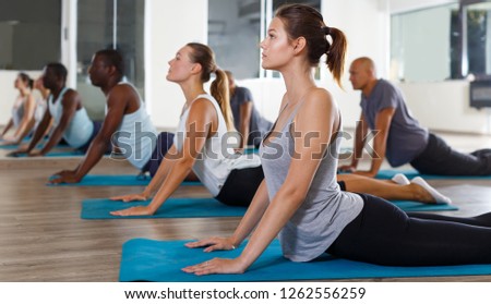 Glad women and men exercising during yoga class in modern fitness center