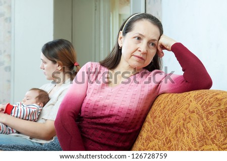 Sad mother against adult daughter with baby after quarrel at home. Focus on mature