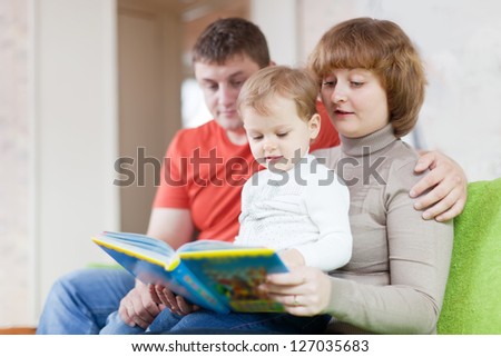 Happy parents with child looks the book in home interior