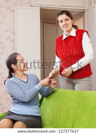 woman gives money to her mature mother on sofa at home