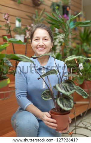 Happy mature woman with Calathea plant in flower store