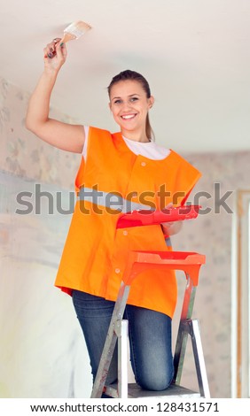 Female house painter paints the ceiling with a brush