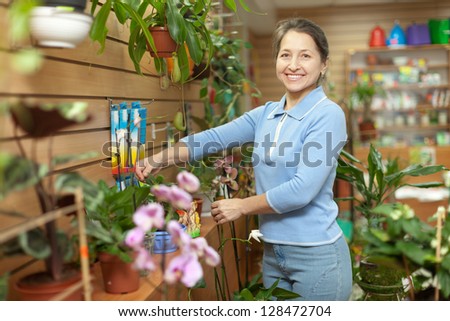 Happy mature woman with  Kalanchoe plant surrounded by different flowers in flower store