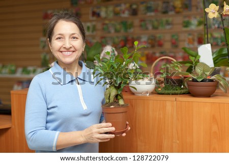 Happy mature woman with  ficus plant (Bonsai) in pot at flower store