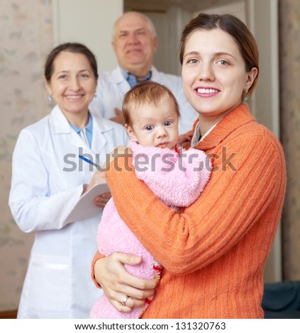 Portrait of happy mother holding baby with doctors in background