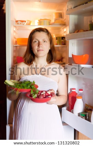 pregnant woman with fresh vegetables near fridge at home