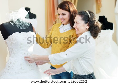 mother  with daughter chooses bridal gown at shop of wedding fashion. Focus on mature