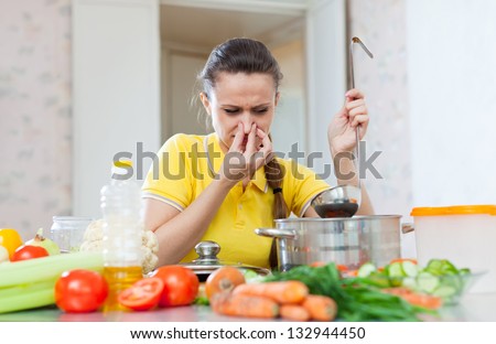woman holding her nose because of bad smell from soup in pan at kitchen