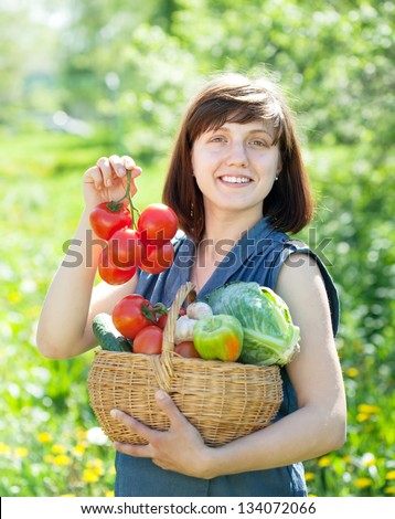Happy young woman with basket of harvested vegetables in garden