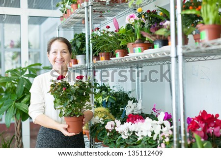 Happy mature woman chooses flower at flower store