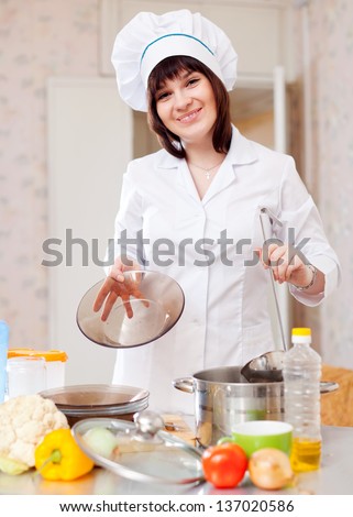 cook woman with ladle pours soup from pan
