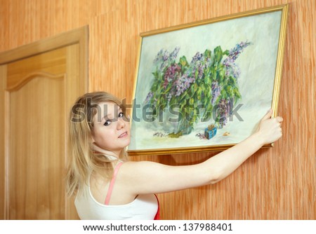 Young woman  hangs the art picture on wall at home