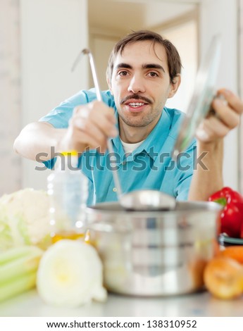 caucasian handsome guy with ladle cooking vegetables soup at kitchen