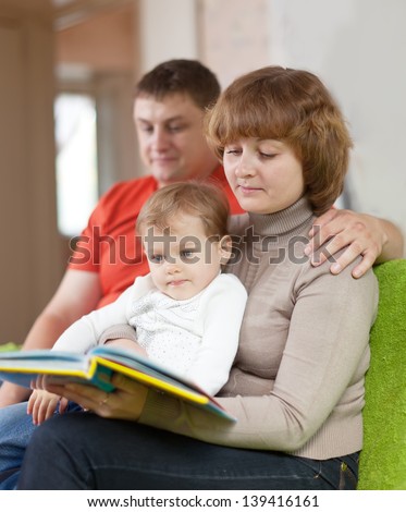 parents with child looks the book in home interior