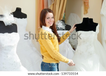 Smiling pretty bride chooses wedding dress in bridal boutique