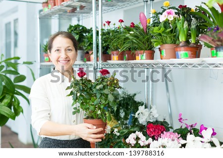 Happy mature woman with roses plant in flower store