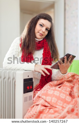 beauty woman reads e-book near oil heater in home