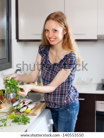 Smiling woman with raw fish and parsley in the kitchen