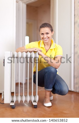 Happy woman near oil heater in home