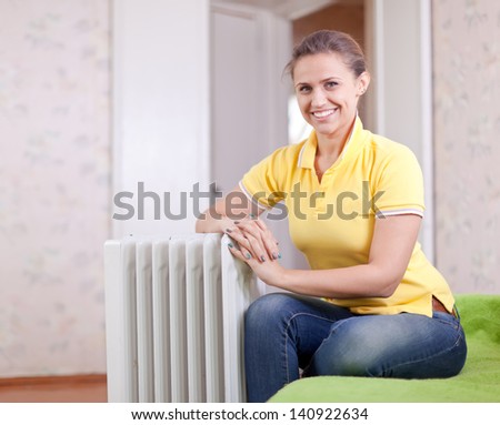 Happy woman near oil heater in home