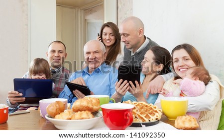 Happy family of three generations or group of friends with electronic devices over tea at home