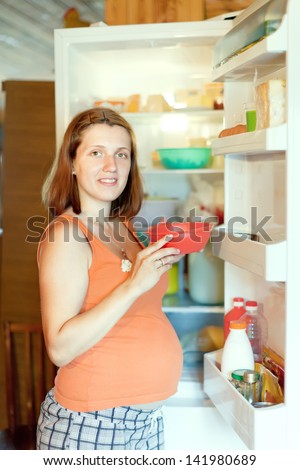 pregnant woman with dish  near refrigerator  at home