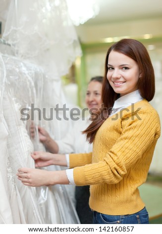 Mature mother  with daughter chooses white gown at shop of wedding fashion