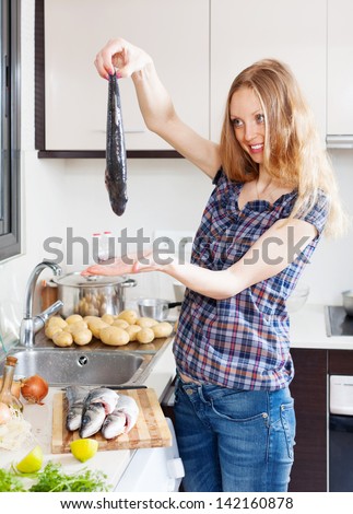 Smiling blonde woman with raw fish  in home kitchen