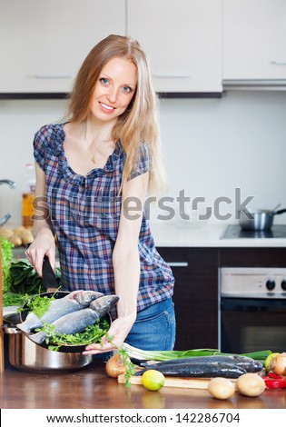 Smiling woman cooking lubina  in skillet at home kitchen