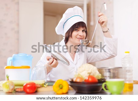cook woman  tasting soup with ladle from pan in kitchen