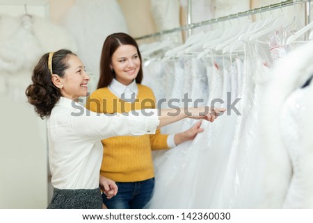Shop assistant  helps the bride in choosing bridal dress at shop of wedding fashion