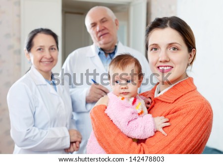 Portrait of happy mother with three months baby in arms against pediatrician doctors in background
