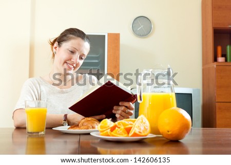 Positive young woman with book during breakfast with juice