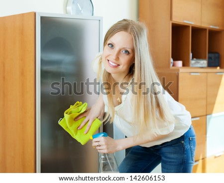 Happy blonde girl cleaning  glass door of furniture